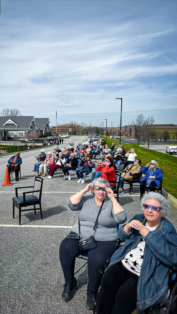 A lively scene unfolds in the parking lot as Vitalia Rockside senior living residents and employees gather in chairs, eagerly observing solar eclipses.