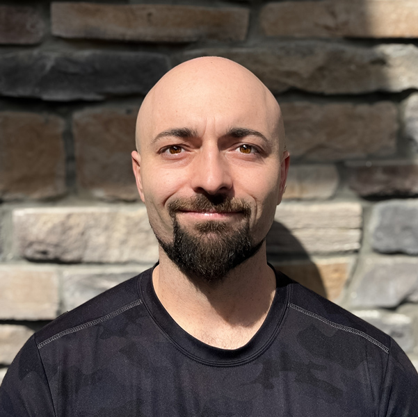 Alexander 'Alex' Bratsch, Culinary Director at Vitalia Rockside, standing against a textured stone wall, smiling with sunlight highlighting his face.