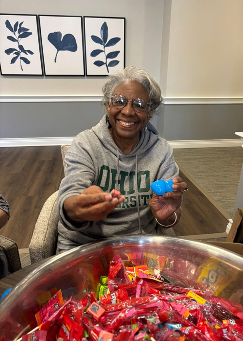 Smiling woman filling a blue plastic egg with candy for an Easter event.