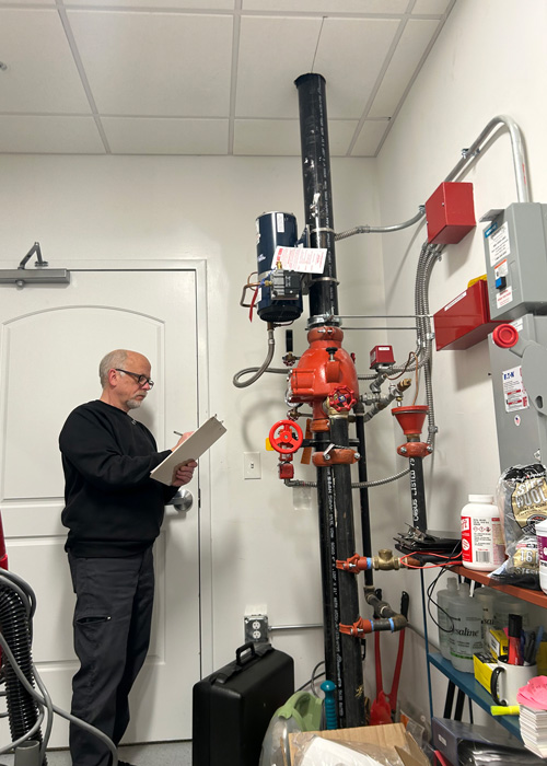 Maintenance team member performing a fire system inspection in a utility room.