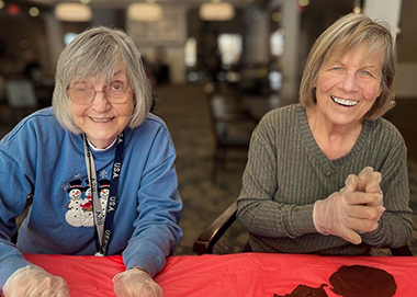 Two senior women at Vitalia Rockside smile while working on a project.