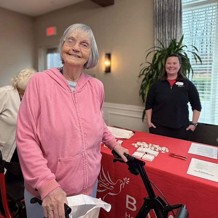 A senior woman smiles, visiting a table offering wellness materials during a wellness event.