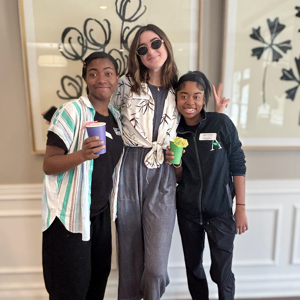 Three women on the team at Vitalia Rockside Senior Living smile for a photo in an elegantly decorated common space.