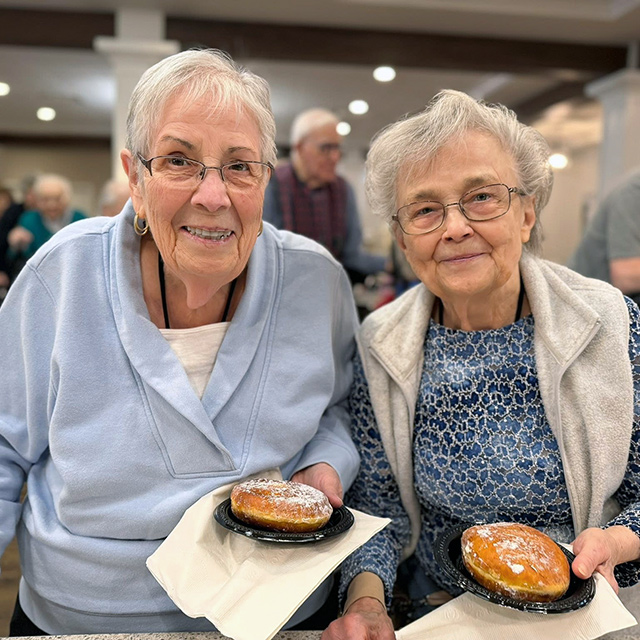 Two senior women smile during an event, holding large donuts, at Vitalia Rockside.