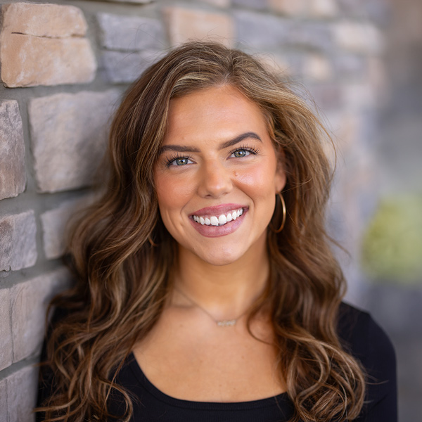 Christine Crabiel, Senior Living Director at Vitalia Rockside, smiling in a professional headshot with long wavy brown hair, gold hoop earrings, a black top, and a softly blurred stone wall background.
